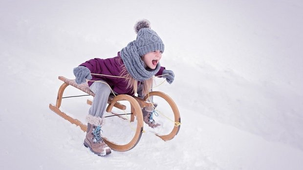 Kind fährt Schlitten im Schnee bei den Ferienwohnungen